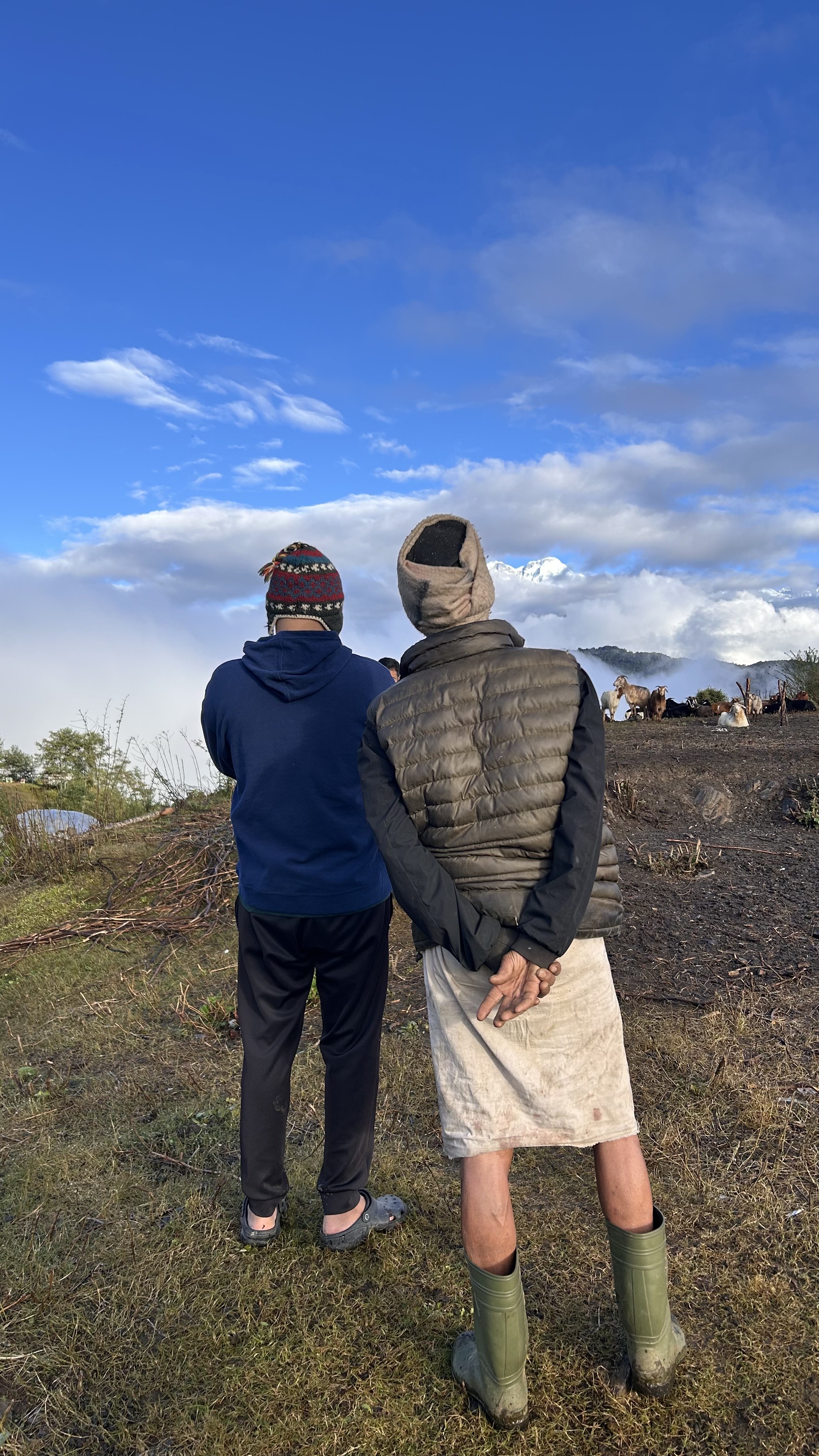 Two individuals stand side by side, facing a wide open sky with scattered clouds.