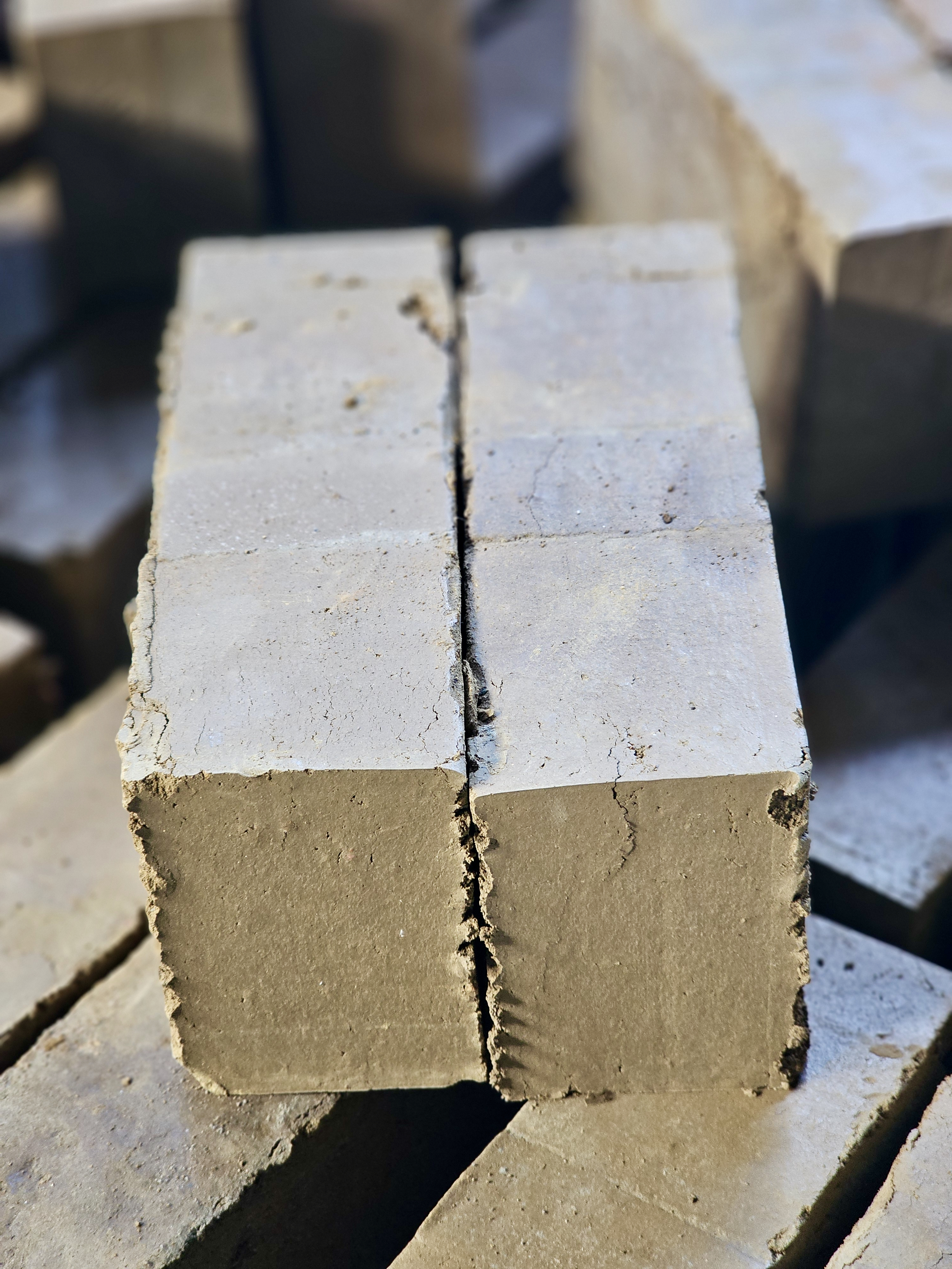 Freshly cut interlocking mud bricks arranged in a stack. Their rough edges and natural texture show the raw stage before drying. Captured in Perumanna, Kozhikode, Kerala.
