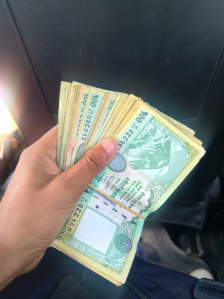 A close-up of a person’s hand holding a stack of Nepal note, mainly featuring green currency, with visible denominations and a design that includes elements like mountains