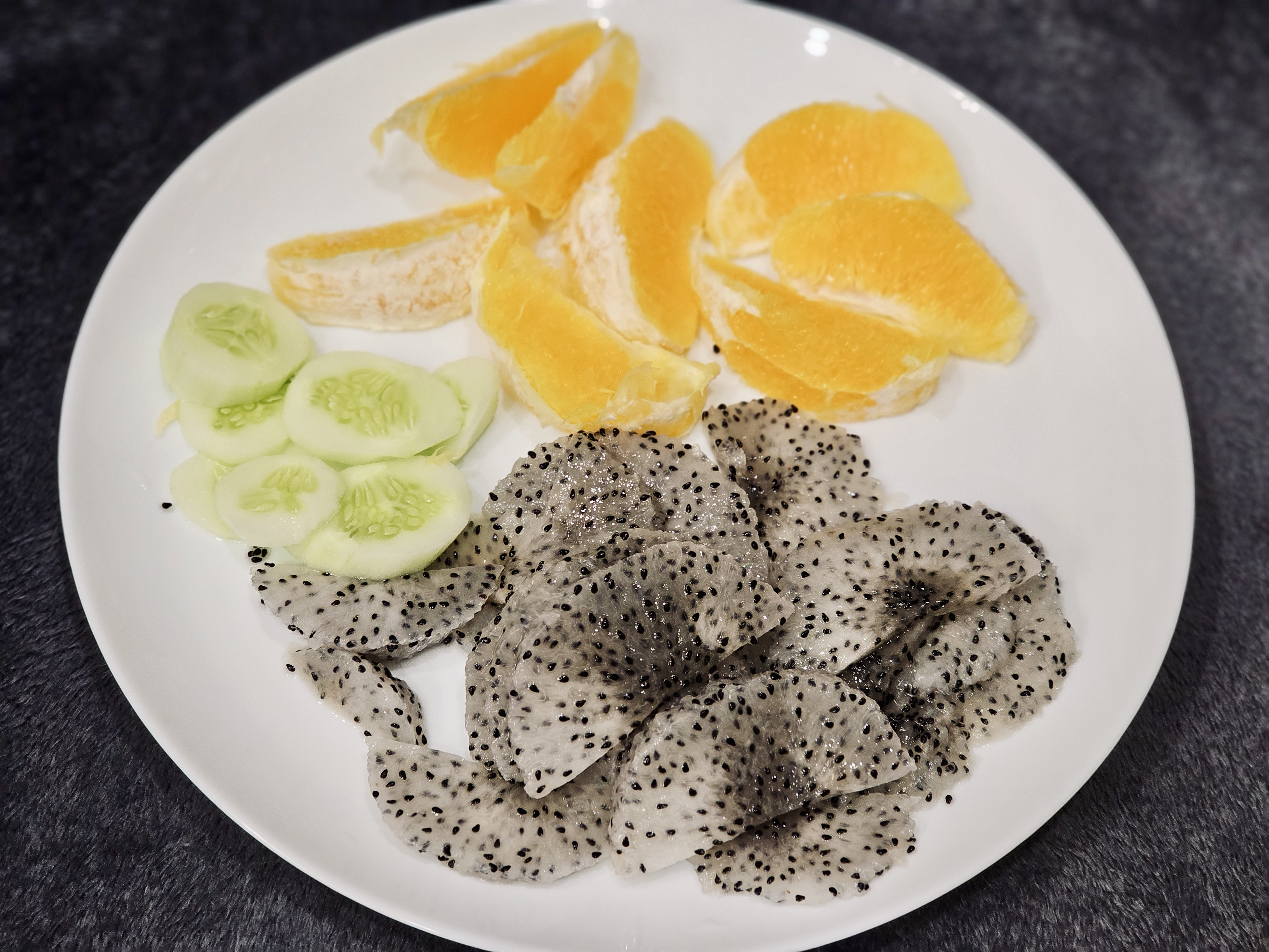 Bright orange slices, crisp cucumbers, and soft dragon fruit are neatly arranged on a white plate in Perumanna, Kozhikode, for a clean, refreshing food shot.
