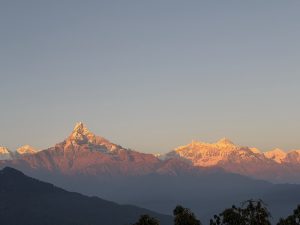 A panoramic view of majestic snow-capped mountains during sunset, with warm hues highlighting the peaks. 