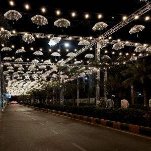 Decorative street lighting with illuminated hanging umbrellas creating a festive night atmosphere along a city road.