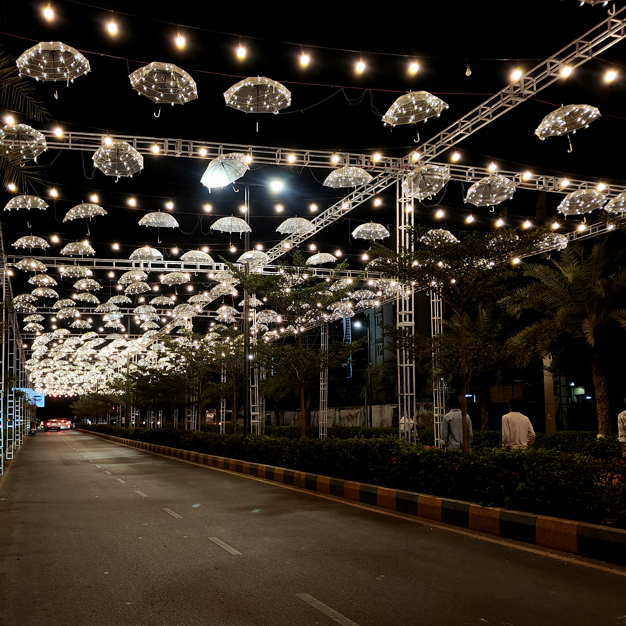 Decorative street lighting with illuminated hanging umbrellas creating a festive night atmosphere along a city road.