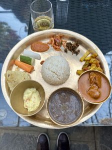 A brass platter with rice, gravies, lentils, vegetables, bread, and a creamy dip.