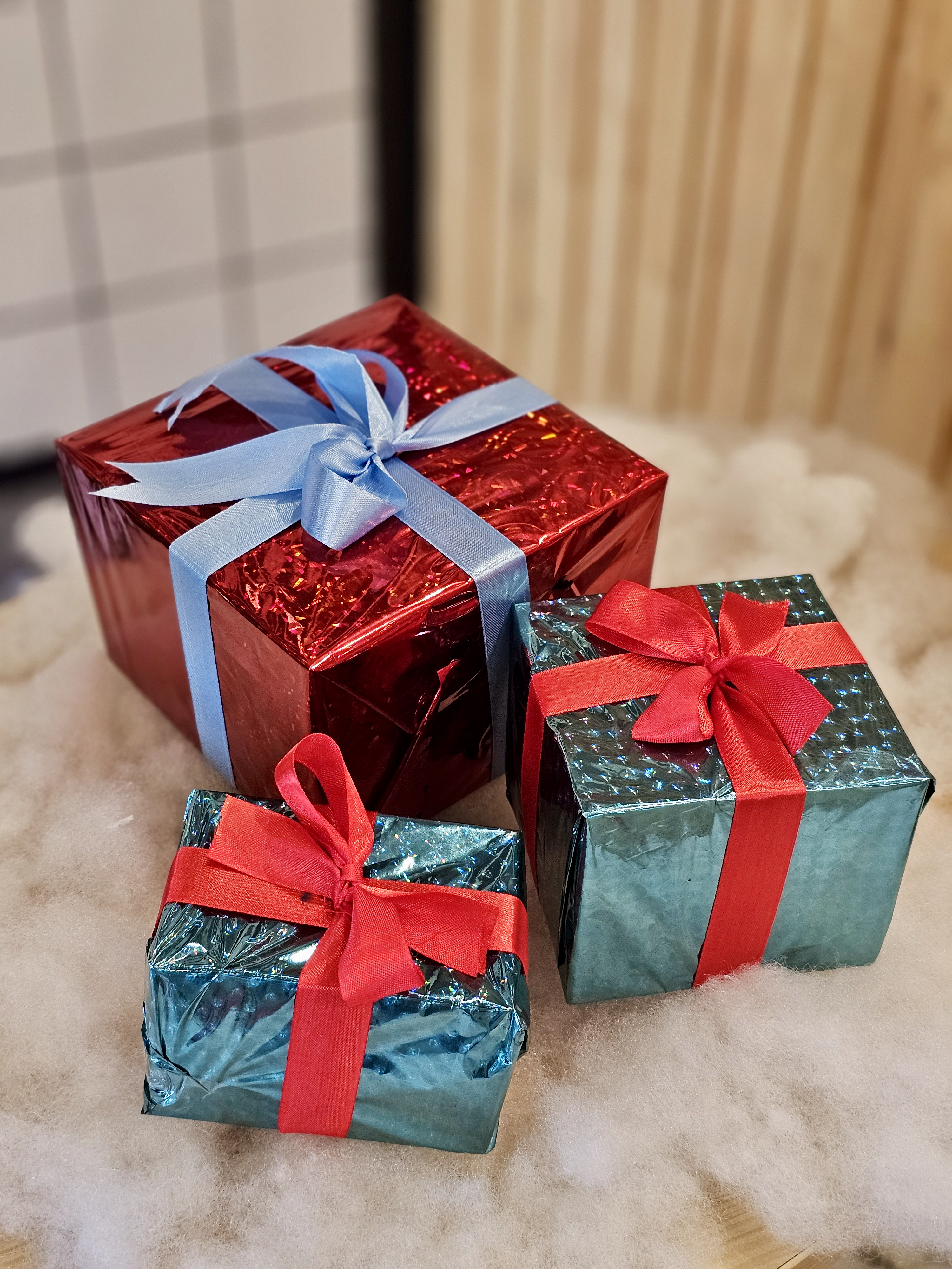 Colourful gift boxes wrapped in shiny paper with ribbons, arranged on a soft white surface. The warm lighting adds a cozy, festive mood. This joyful Christmas scene was photographed in Kozhikode, Kerala. 