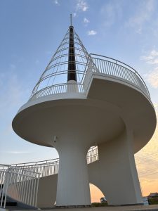 A modern circular observation tower with a conical top, white railing, and spiral staircase at Toyomi Beach, Kujukuri Town, Chiba.