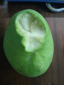 

A green mango with a bite taken out of it, sitting on a wooden surface.