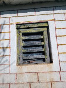 A close-up view of a small, wooden window set into a white and beige wall