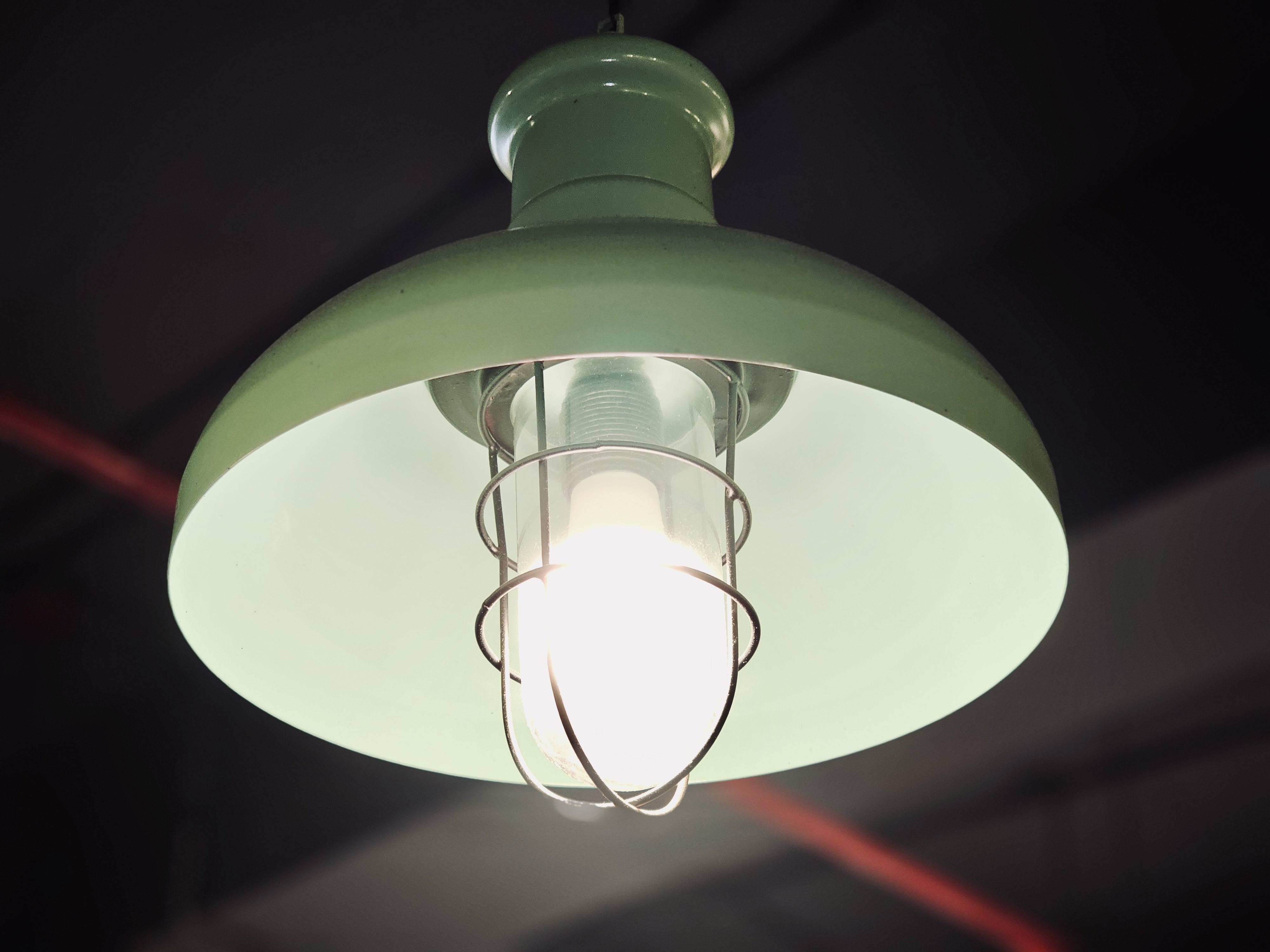 A green metal hanging lamp glowing softly indoors, creating a calm and warm mood. The simple design and focused light highlight everyday interior details, captured in Kozhikode, Kerala, with a clean and minimal background. 