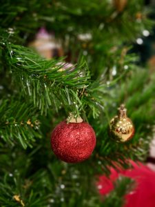 A shiny red Christmas ornament hanging on green artificial pine branches. The soft background blur adds depth and festive warmth. This indoor festive detail was captured in Kozhikode, Kerala, during seasonal decorations. 
