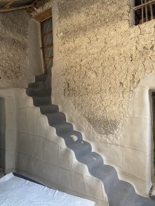 A steep, narrow staircase with dark steps climbs a rugged, textured wall in an old, rustic building.