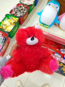 A bright red plush bear with pink accents is being held by a hand