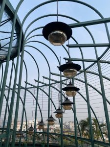 A view of a modern architectural structure featuring a series of curved metal beams with hanging light fixtures. 