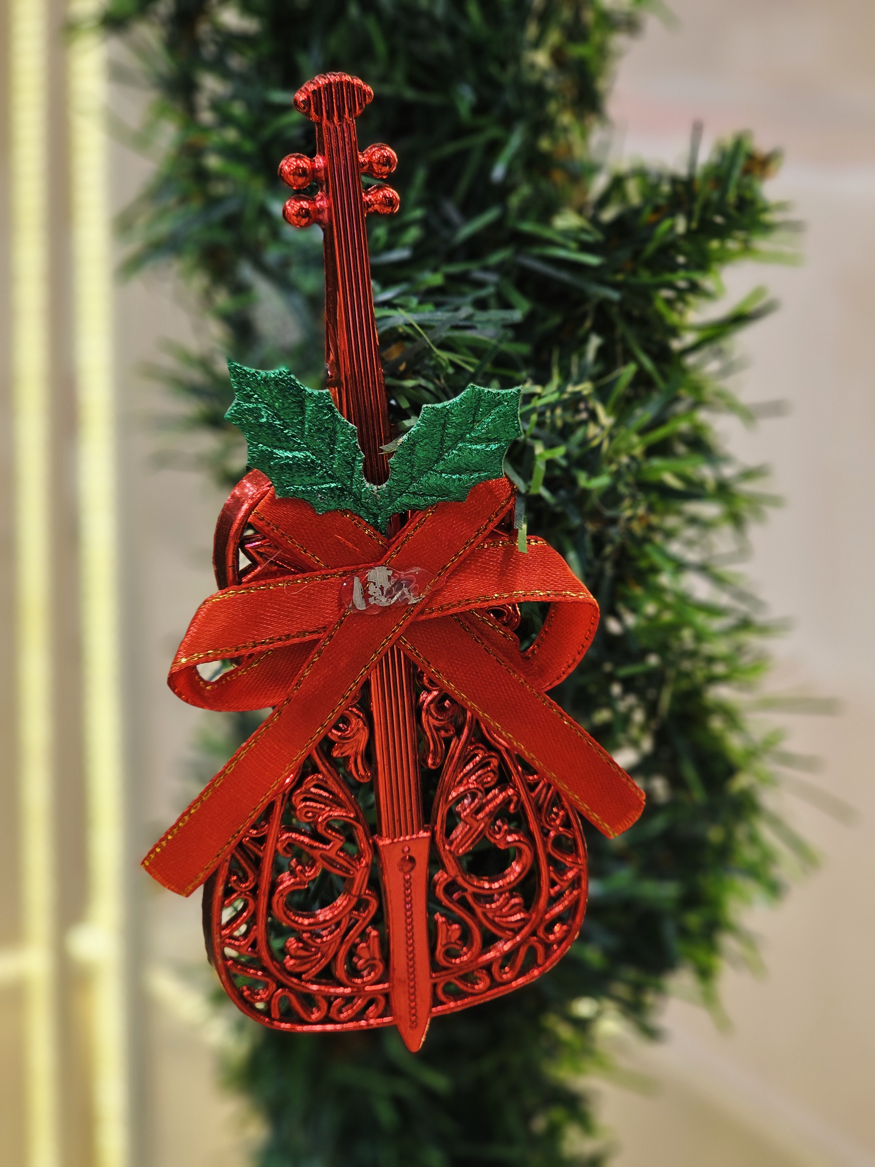 A decorative red violin-shaped ornament with a ribbon, hanging on a Christmas tree. Shot in Kozhikode, Kerala, the image captures festive spirit, holiday décor, and fine details with a pleasing background blur and vibrant seasonal colors. 