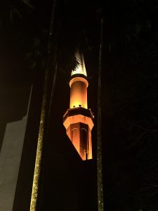 A brightly lit minaret rises into the night sky, surrounded by tall palm trees Masjid Sultan Ismail, Night View, Universiti Teknologi Malaysia.
