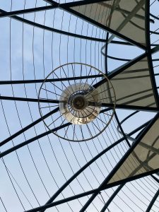 

Looking up at a geometric glass ceiling with a circular chandelier and sky beyond.