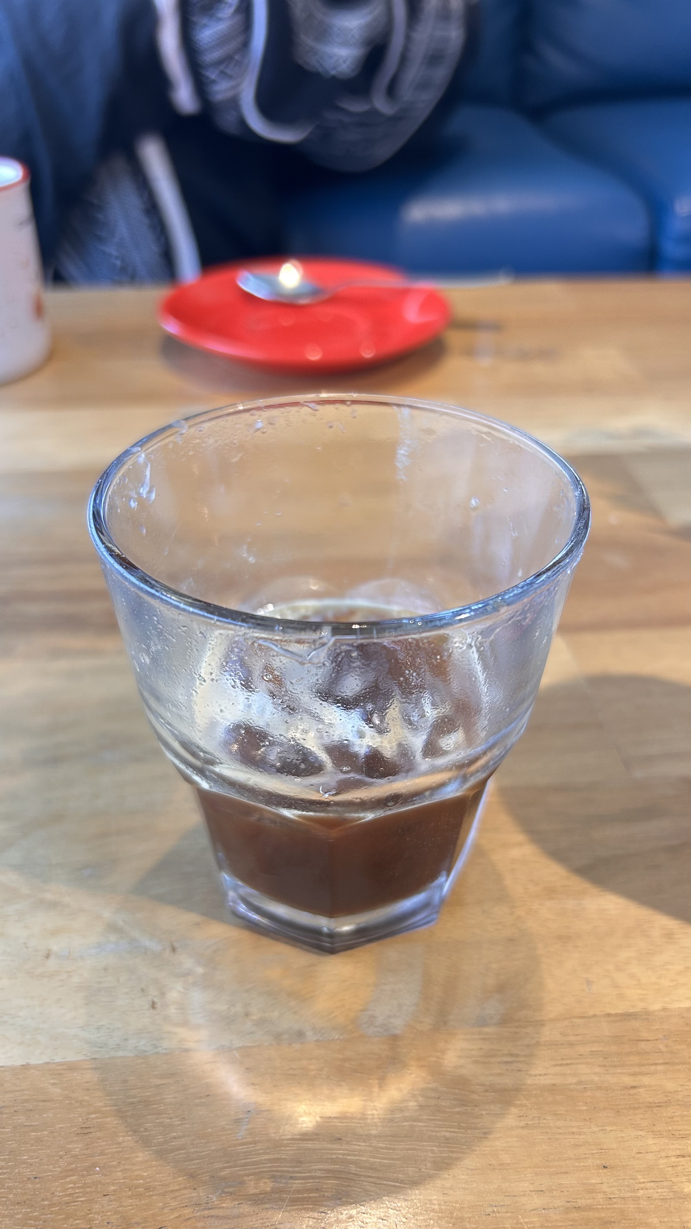 A clear glass of dark coffee with condensation sits on a wooden table.