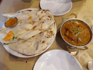 A vibrant display of Indian food showcasing a soft Nan bread with a small bowl of tomato sauce and chicken curry, placed on a table with two empty white plates.