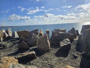 Close-up of jagged rocky terrain by a calm sea under a bright blue sky with scattered clouds in Newport, Rhode Island.