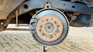 A close-up view of a vehicle's brake system, featuring a rusted brake disc and caliper.