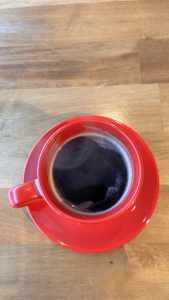 A top-down view of a red coffee cup filled with dark coffee on a wooden table.