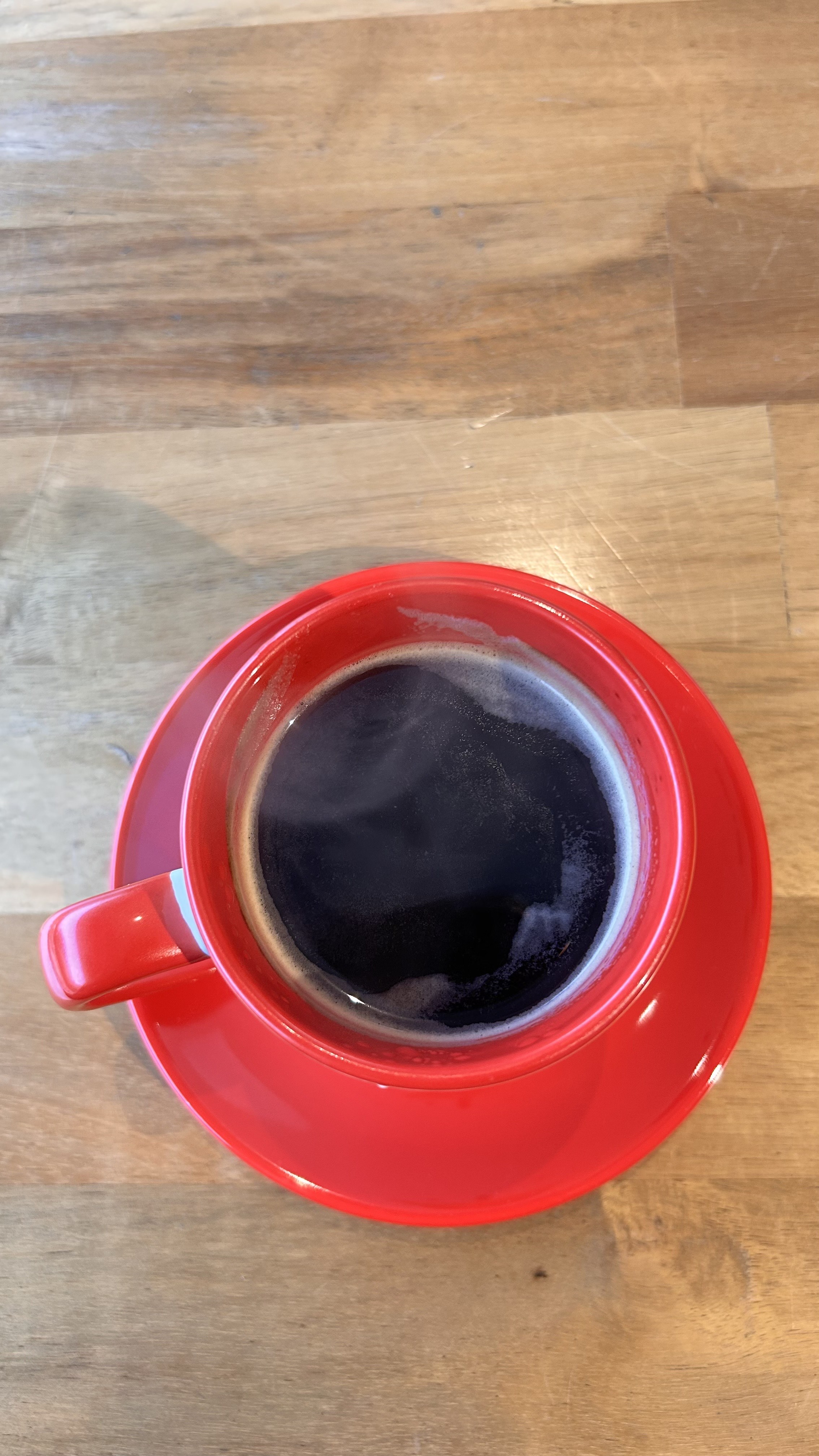 A top-down view of a red coffee cup filled with dark coffee on a wooden table.