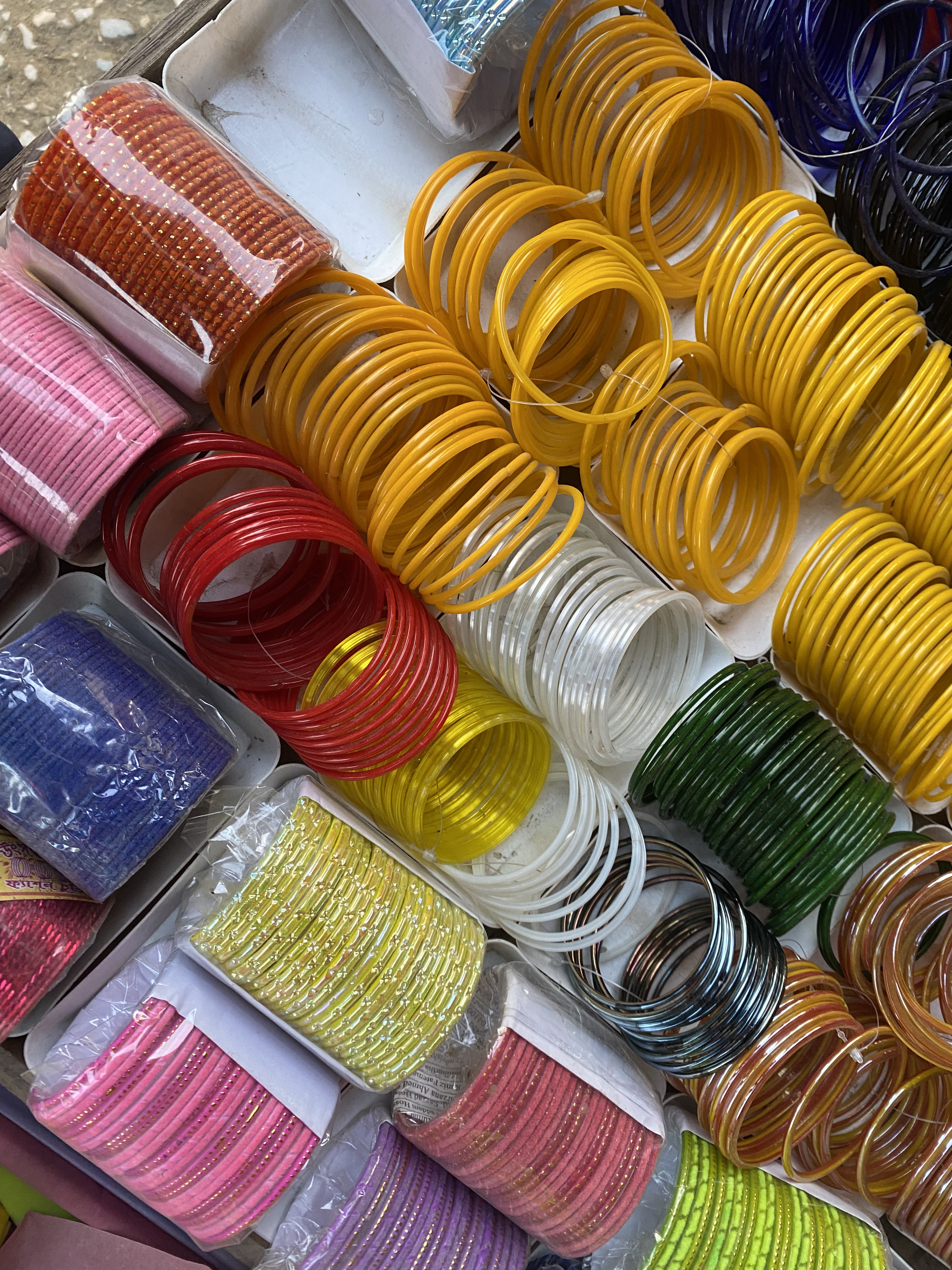 A vibrant array of colorful plastic bangles neatly organized in a display. Shades range from yellow, red, and pink to green, creating a lively, festive feel.