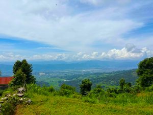 A panoramic view of a lush green landscape with rolling hills and valleys under a partly cloudy sky