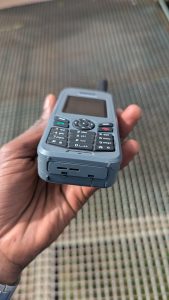 A human hand holding a satellite phone, which displays all the keypad letters and numbers.
