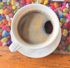 A top-down view of a cup of coffee on a white saucer, placed on a wooden surface.