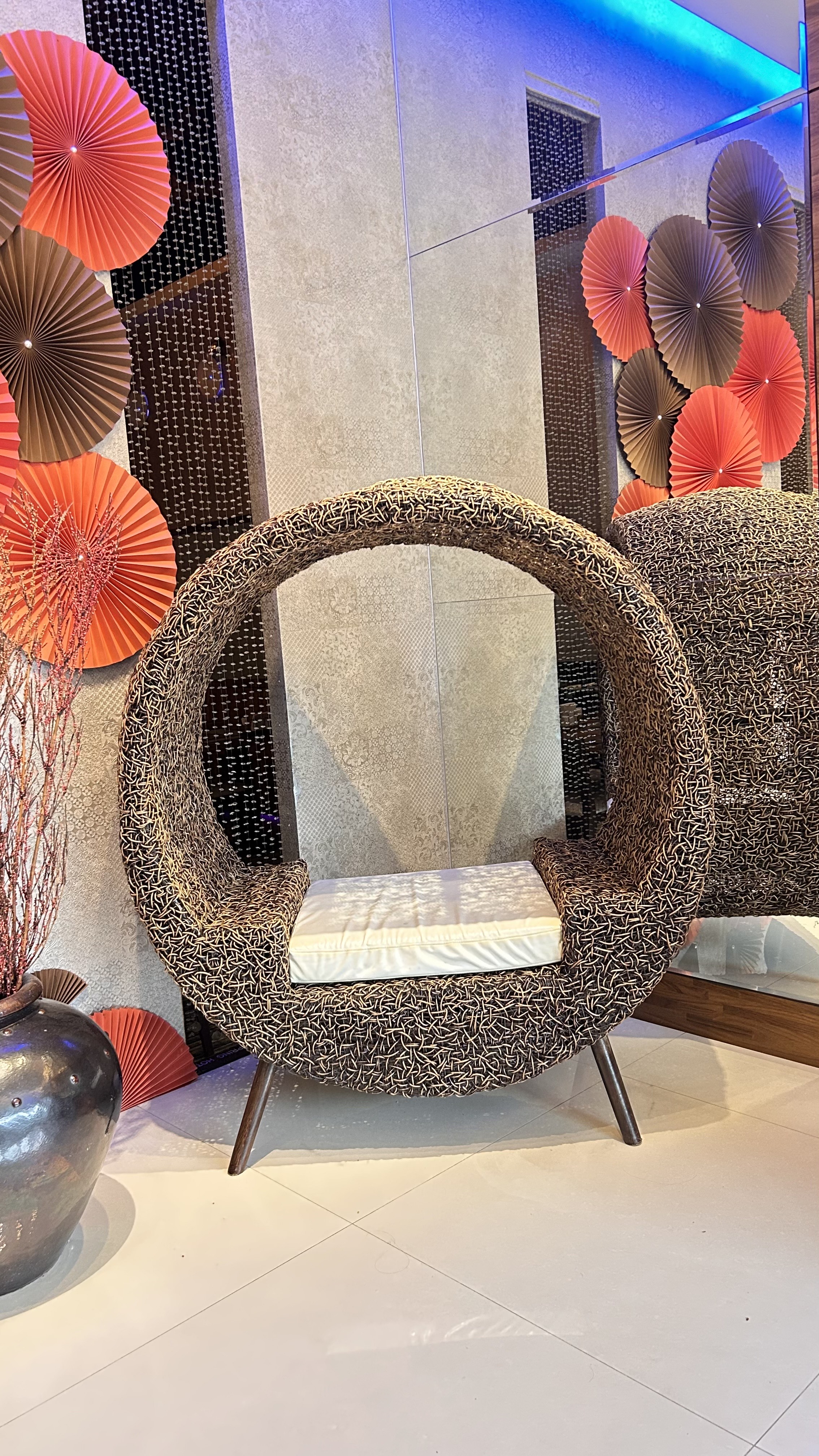 A unique circular chair with a textured brown woven design and a white cushion sits against a stylish backdrop.