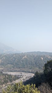 A scenic view of a mountainous landscape featuring a valley with a winding riverbed surrounded by trees and vegetation. 
