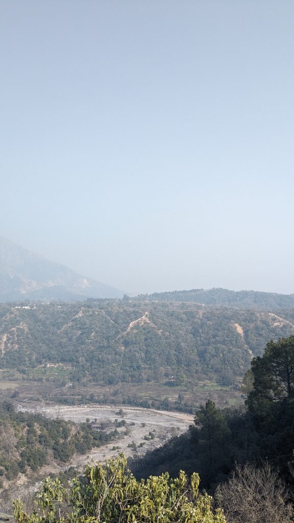 A scenic view of a mountainous landscape featuring a valley with a winding riverbed surrounded by trees and vegetation.