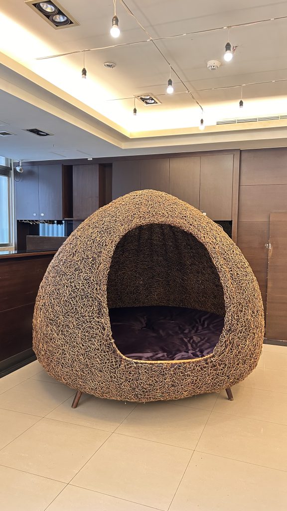 A large, dome-shaped seating structure made of woven material resembling twigs or vines, featuring a purple cushion inside.