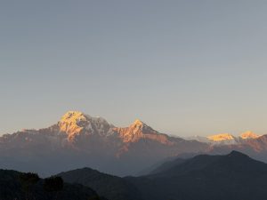 A panoramic view of majestic snow-capped mountains under a clear sky, with soft sunlight illuminating the peaks