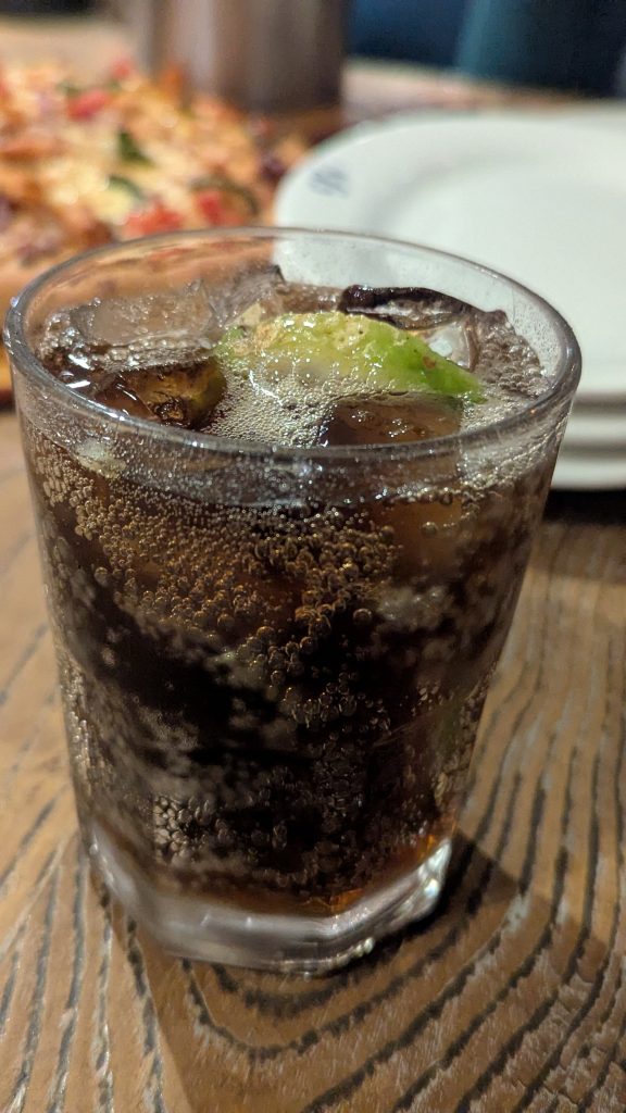 A cold Coke in a glass with ice and a lemon slice