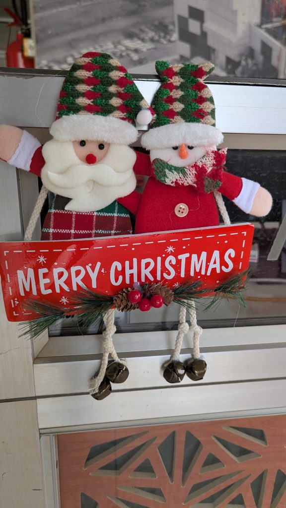 Christmas display with Santa, a snowman, and a “Merry Christmas” sign on a glass door.