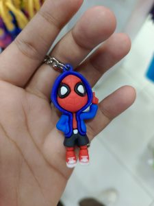 A hand is holding a small keychain figure of a cartoon character styled as a superhero. 