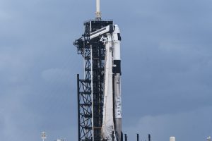 A 70-meter-tall SpaceX Falcon 9 rocket with a rounded Dragon spacecraft on top awaits the launch of the Axiom Mission 4 crew. The sky is clear and sunny.