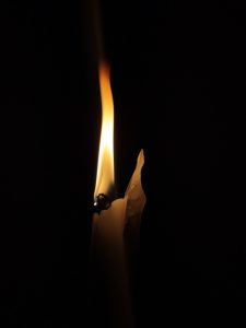 A single white candle is illuminated against a black background. 