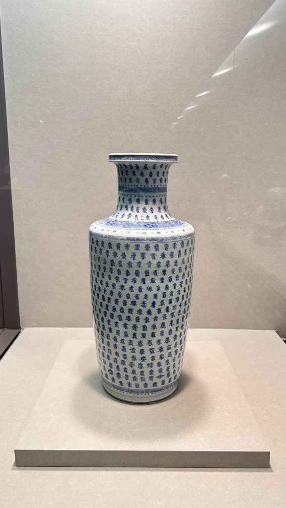 A tall, intricately designed vase featuring a white background and detailed blue patterns, including floral motifs and Chinese characters.