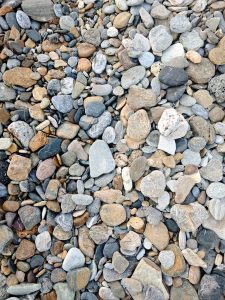 A close-up view of various smooth pebbles and stones scattered on a surface. The stones display a range of colors including shades of gray, brown, beige, and white, with diverse shapes and sizes creating a textured, natural pattern.