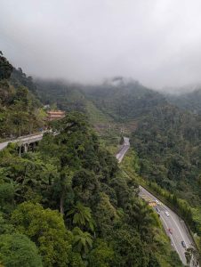 A misty mountainous landscape in Genting Highlands, Malaysia, with lush forests and a winding road with a few vehicles.