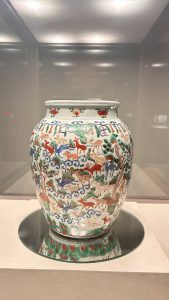 A decorative ceramic jar with a rounded body, featuring intricate illustrations of deer and trees in vibrant colors, including red, green, and blue, against a white background