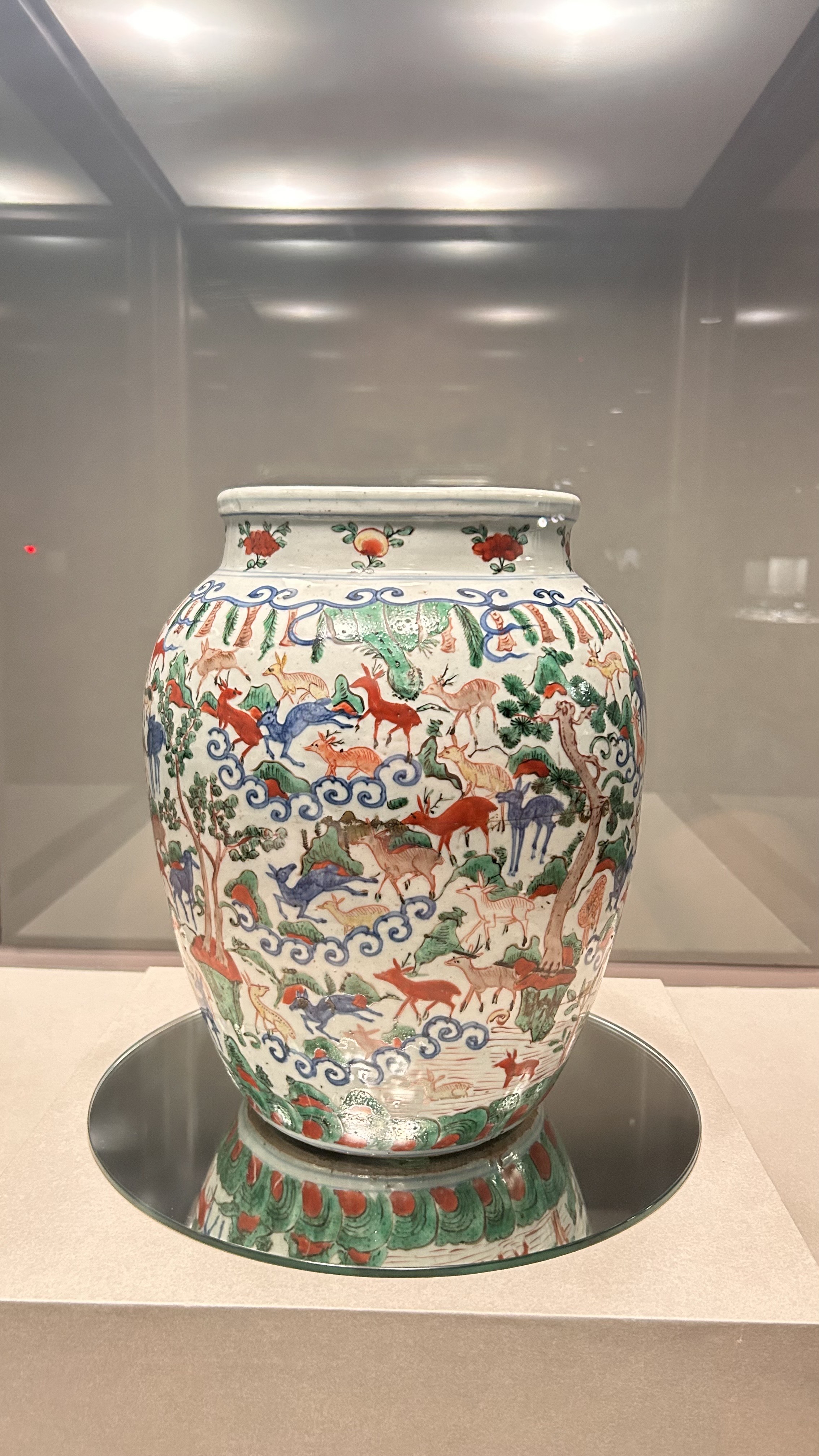 A decorative ceramic jar with a rounded body, featuring intricate illustrations of deer and trees in vibrant colors, including red, green, and blue, against a white background