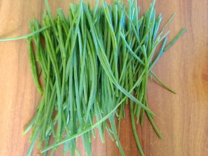 A bunch of fresh green onion leaves with long, thin stems on a wooden surface.