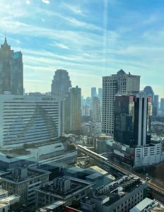 High-angle view of Bangkok city skyline with modern office buildings and condominiums, featuring a skytrain running through the city under a clear blue sky.