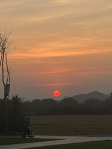 A glowing red sun sinks behind the hills as soft orange and pink clouds drift across the evening sky.