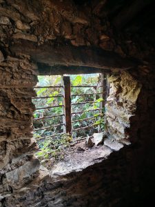 A weathered stone wall featuring an arched window illuminated by natural light. 