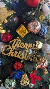 A close-up view of a decorated Christmas tree, featuring a mix of colorful ornaments, including red, gold, silver, blue, and green. 